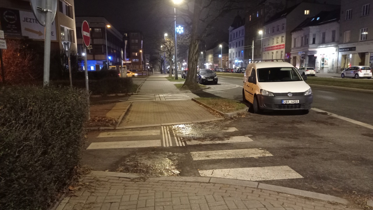 Propadlý asfalt s loužemi na přechodu vedle domu Sokolovská 179