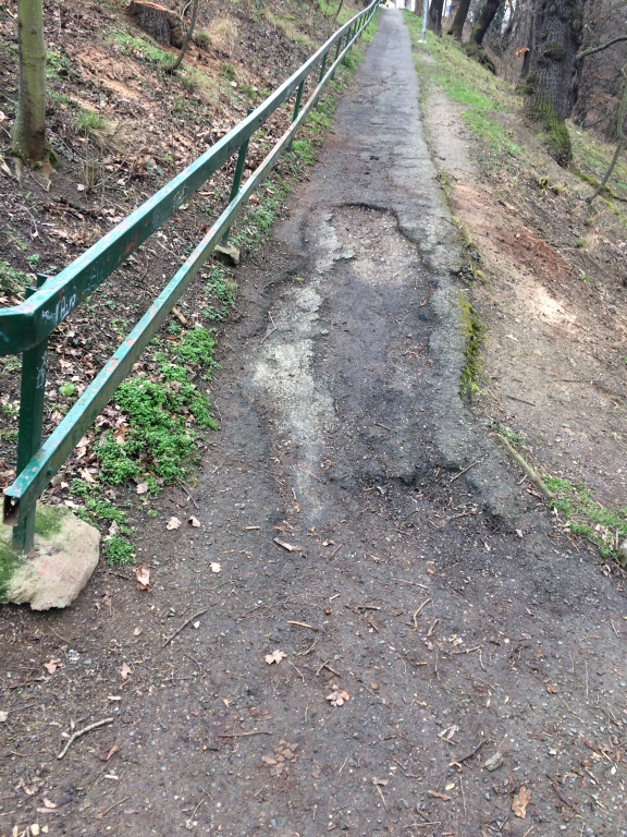 Hluboký výmol v celkově rozbitém chodníčku nad parkem Jezerka